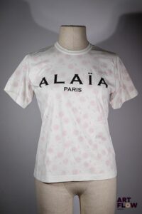 ALAIA Paris Tee shirt en coton blanc à motif de fleurs rouges imprimé du logo "ALAIA Paris" sur le devant. Taille présumée S/M. Très bon état général.