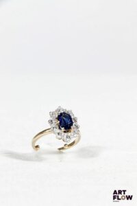 Bague en or jaune 750‰ et platine, de forme marguerite légèrement oblongue, composée au centre d’un saphir naturel d’un magnifique bleu soutenu, de forme ovale (8.7x6.2mm), pour un poids estimé de 1.80 carat, monté sur six griffes ; mis en valeur par un entourage de dix diamants taille brillant, sertis sur griffes, de qualité estimée G SI, pour un poids total de 1.36 carat environ. Très belle monture bicolore faite à la main de la deuxième moitié du XXe siècle. Présence de boules sur l’anneau pour éviter que la bague ne tourne une fois portée au doigt. (Très légères usures sur le saphir, un diamant légèrement égrisé) Diamants : 1.36 carat environ Saphir : 1.80 carat environ Poids : 5.55 g Tour de doigt : 52 avec les boules, convient pour un tour de doigt 54/55