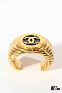 CHANEL Bracelet jonc en métal doré avec le double C sur fond noir en son centre. Diamètre : 5,5 cm environ Usures à la dorure