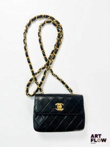 CHANEL Mini Timeless Sac Chanel porté épaule en cuir noir, bandoulière en métal doré entrelacée de cuir, bijouterie en métal doré, intérieur cuir. Avec dustbag. 10 x 14 x 4,5 cm env. Petites usures, dont plis naturels du cuir et rayures sur la bijouterie, et usures à la bandoulières. Intérieur en l’état (importantes usures)