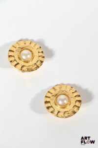 CHANEL Paire de clips d'oreille en métal doré orné au centre d'une perle synthétique Signés Diamètre : 3 cm