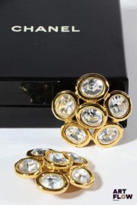 CHANEL Paire de clips d'oreilles en métal doré formant des fleurs stylisées ornées de strass. Dimensions : 4,5 cm environ Dans leur boîte d'origine.