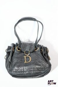 CHRISTIAN DIOR 2008 Sac modèle Drawstring en agneau noir surpiqure motif cannage, orné d'un D en métal patiné vieux or. Anse formant cordon de serrage en cuir, anneaux et bijouterie également en métal patiné vieux or. Doublure en tissu satiné rouge monogrammé avec deux poches plaquées et une poche zippée. 35 x 25 x 17 cm Bon état général malgré quelques défauts (usures d'usage, taches à l'interieur)