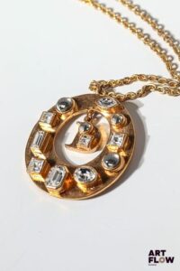 Christian DIOR boutique Sautoir en métal doré avec pendentif en forme de disque, orné d'imitations de diamants en serti clos et D de Dior en pampille. Longueur totale : 44 cm