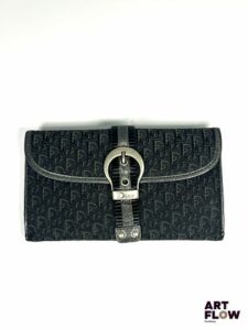 Christian DIOR Pochette portefeuille en toile noir monogrammée, fermeture bouton pression et agrémenté sur le devant par une boucle de ceinture décorative en métal. Dimensions : 10 x 18 cm