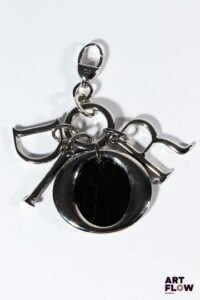 CHRISTIAN DIOR Porte-clé avec charms en métal argenté et pièce en cuir vernie noir. Signé