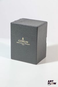 CORUM Boite en cuir gris et sur boite en carton grise Emblème de la marque sur la boite en métal doré 12 x 8,5 x 7 cm pour la boîte Traces d'usage, bon état général