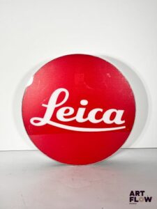 Enseigne lumineuse publicitaire sur plexiglas Leica. Dimensions : 53 x 35 cm Fonctionnelle - État général excellent. Fourni avec son alimentation murale.