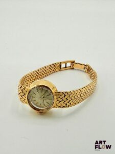 ETERNA Montre bracelet de dame en or 750/°°, à mouvement mécanique à remontage automatique, masse oscillante en or, le boîtier rond à cadran à fond champagne, index bâtons, aiguilles dauphine Poinçon Paul Franck et fils Diamètre 16 mm Longueur du bracelet : 14,5 cm env. Poids brut : 31,86 gr Bon état général (maillons endommagés) Fonctionnelle au moment de la rédaction du catalogue, mécanisme non garanti. La marque Eterna est une maison horlogère suisse fondée en 1856, reconnue pour ses innovations techniques, notamment l’introduction du rotor à roulement à billes en 1948, qui a révolutionné les montres automatiques. Elle s’est aussi illustrée avec la collection KonTiki, inspirée d’une célèbre expédition maritime. Aujourd’hui, Eterna reste associée à la précision suisse et à un riche héritage horloger. Le poinçon de maître permet également d’en apprendre davantage sur cette pièce. En effet, la manufacture Paul Franck était spécialisée dans la fabrication de boîtiers en métaux précieux à Taverny. Dans les années 1960, les villes de Taverny et de Saint-Leu-la-Forêt constituaient le principal centre de fabrication de boîtiers de montres de la région parisienne.
