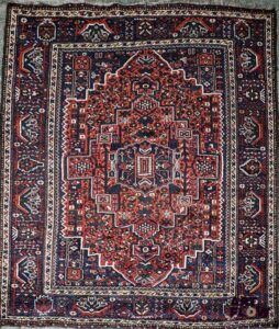 IRAN - SHIRAZ Tapis en laine à décor dans les tons rouges d'un losange central H. 210 x L. 176 cm (hors franges) Bon état général malgré quelques légers défauts (poussières, petites usures d'usage)