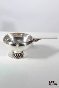 Jean DESPRES (1889-1980) Coupe vide poche ronde sur piédouche en métal argenté évoquant un poêlon. La base soulignée d'une chaine. Signée J. DESPRES à la pointe au revers de la prise et datée 6/7/68 sous la base. Haut. : 7,5 cm L. : 21,5 cm Dans sa boite d'origine Rayures d'usage