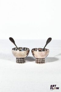Jean DESPRES (1889-1980) Paire de salerons en métal argenté sur talon orné d'un triple rang de perles. Avec deux petites cuillères. Signé "J.Despres' à la pointe sur le corps. H. 3 x Diam. 4 cm Petites rayures d'usage.