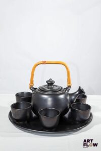 JEAN MARAIS Service à thé en céramique à glaçure noire comprenant : - 1 plateau rond. D. 32 cm - 1 théière avec anse en osier (petite egrenure au bec verseur). Signée. H. 21,5 cm - 6 tasses. H. 6 cm Très bon état général.