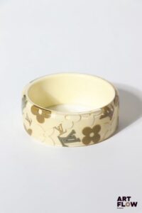 LOUIS VUITTON Bracelet "Inclusions" en résine a fond crème et motifs gris et taupe. Diamètre intérieur : 6,8 cm H. : 3 cm Traces internes à noter.
