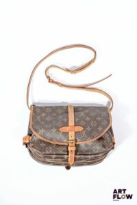 LOUIS VUITTON Sac besace modèle Saumur en toile Monogramm à double sacoches, fermeture sangles, pattes de serrage, anse bandoulière réglable. Deux compartiments de part et d'autre. Dim : 30 x 20 cm Bon état général malgré quelques défauts (usures d'usage, petites taches)