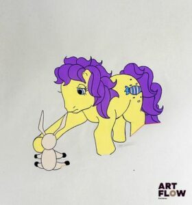 Mon Petit Poney (My Little Pony) Sweetie Drops Cellulo à l'encre et à la gouache représentant Sweetie Drops tenant un jouet Série d’animation et franchise américaine produite par Hasbro. « My Little Pony met en scène des poneys colorés évoluant dans un univers féerique où l’amitié, la solidarité et la bienveillance occupent une place centrale. Devenue une franchise emblématique depuis les années 1980, elle séduit par son esthétique vive, son univers enchanteur et ses messages positifs destinés à un large public. » Dimensions : 26,5 x 31,5 cm