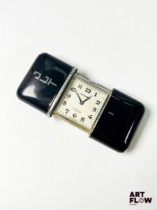 MOVADO Modèle Ermeto Montre de voyage en bakelite, à mouvement mécanique à remontage glissière, le boîtier rectangulaire à cadran à fond argenté, aiguilles losange bleuies, index appliqués en chiffres arabes bleuies Années cira 1930 Dimensions : 33 x 43 mm Bon état général Monogrammée « JLT » Fonctionnelle au moment de la rédaction du catalogue, mécanisme non garanti. La Movado Ermeto est lancée dans les années 1920 par la marque suisse Movado, conçue comme une montre de voyage compacte et élégante. Elle se distingue par son boîtier coulissant protecteur et son style Art déco, devenant un accessoire prisé pour sa robustesse et son raffinement. Expert : Monsieur Alexis Francis-Boeuf