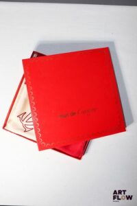 MUST DE CARTIER Carré en soie ivoire à motif de bijoux.Bordure rouge rubis. 85 x 85 cm. Dans sa boite d'origine. Bon état général malgré quelques défauts (tâches).