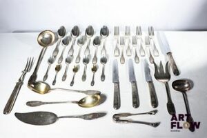 Partie de service de 93 pièces en argent massif à décor néoclassique comprenant : - 12 couverts de table (12 fourchettes et 12 cuillères) - 12 grands couteaux - 2 couverts à découpe - 1 louche - 1 cuillère à sauce - 2 couverts à salade en argent vermeillé - 12 petites fourchettes - 12 petites cuillères - 2 couverts de service à dessert - 12 cuillères à dessert - 1 pince à sucre - 12 cuillères à café en argent vermeillé Circa 1900 Poinçon Minerve 1er titre (950/1000) Chiffré MB Poids brut total : 5190,77 g Poids : 4410,1 g (sans les couteaux)