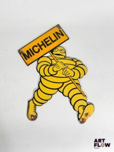 Plaque émaillée Michelin représentant le bonhomme Michelin portant une pancarte Dimensions : 28 x 22 cm Petits éclats et traces de rouille Reproduction moderne