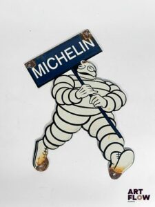 Plaque émaillée Michelin représentant le bonhomme Michelin portant une pancarte Dimensions : 28 x 22 cm Petits éclats et traces de rouille Reproduction moderne