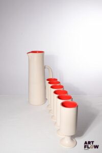 POL CHAMBOST (1906-1983) Service à orangeade 2049 en faience émaillée à couverte blanche à l'extérieur, rouge vif à l'intérieur, comprenant un pichet et 6 verres à pied. Pichet incisé "Poterie Pol Chambost, 2049, Modèle déposé, Made in France" et les verres "2049, France PC" H. pichet 30,5 cm H. verres 17 cm Bibliographie : Philippe Chambost, "Pol Chambost, Sculpteur-Céramiste 1906-1983", Somogy Editions d'Art, Paris, 2006, modèle similaire p. 96