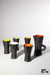 POL CHAMBOST (1906-1983) Service à orangeade 860, comprenant un pichet et 5 verres de forme diabolo, en faience émaillée à couverte noire à l'extérieure et colorée à l'intérieur (jaune, vert et orange). Le pichet et les verres tamponnés en creux "860, Made in France" H. pichet : 19,5 cm H. verres ; 14 cm Bibliographie : Philippe Chambost, "Pol Chambost, Sculpteur-Céramiste 1906-1983", Somogy Editions d'Art, Paris, 2006, modèle similaire p. 115 ; p. 145