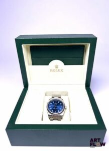 ROLEX Montre bracelet homme en acier, modèle Oyster Perpetual Air King, à mouvement mécanique à remontage automatique, le boîtier de forme ronde à cadran à fond soleillé bleu, index 3-6-9 et bâtons luminescents, lunette lisse, seconde centrale, le bracelet Oyster brossé. Années 2009 Diamètre 34mm Référence 114200 Bon état général Fourni avec un set important comprenant boîte, carte de garantie, tags d'origine, protection de lunette Fonctionnelle au moment de la rédaction du catalogue, mécanisme non garanti. C’est en 1958 que la Rolex Air-King rejoint officiellement la grande famille Rolex, affichant fièrement son nom en italique sur le cadran, une typographie unique dans la marque. Choisie par Hans Wilsdorf lui-même, cette signature distinctive est restée inchangée au fil des décennies, renforçant son identité singulière. Expert : Alexis Francis-Boeuf - AFB Horlogerie