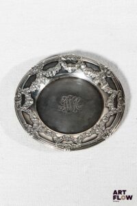 Sous verre en argent, de forme ronde à riche décor de guirlandes de fleurs et noeuds, le centre chiffré. Poids brut : 30 g Diamètre : 9 cm
