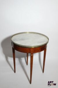 Table bouillotte en bois de placage, posant sur pieds fuselés et cannelés, le plateau en marbre blanc entouré d'une galerie de laiton ajouré. Style Louis XVI. Petits accidents. H 74, d 65 cm Facture de réparation de mai 2011.