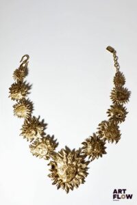 YVES SAINT LAURENT x Goossens Collier en métal doré à décor de soleils. L. 50 cm env. Très légère dédorure sur les anneaux. Modèle rare : sont surtout connus les colliers avec un unique soleil fixé sur collier torque. Le nôtre présente 10 soleils de formes différentes et aux visages plus ou moins esquissés, encadrant un soleil central imposant. Provenance : collection de la famille d'un ami et collaborateur de Robert Goossens.
