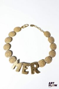 YVES SAINT LAURENT x Goossens Collier MER en métal doré, orné de pastilles texturées et d'un lettrage imposant. Probablement début années 1990. L. 50 cm env. Quelques usures conformes à l'âge de la pièce et dédorures. Provenance : collection de la famille d'un ami et collaborateur de Robert Goossens.