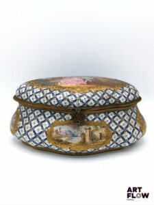 Dans le goût de SÈVRES Boîte en porcelaine ornée sur son couvercle d'une scène galante, et sur ses côtés de scènes lacustres dans le goût du XVIIIe siècle. Marque apocryphe au double L, lettre-date B. H. 9 x L. 21,5 cm x P 14 cm