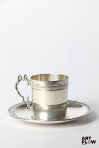 Tasse et sous tasse en argent (poinçon Minerve) de style néo-classique à décor de frises de feuilles d'eau, l'anse de la tasse ornée d'un noeud. Poinçon de maître Henri Gauthier, 1902/1920, 29 rue Beaubourg, Paris Poids total : 177,21 gr