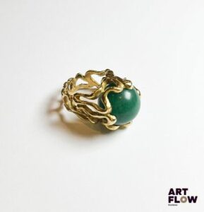 Bague en or jaune 750‰, poinçon tête d’aigle, composée d’un corps entièrement contourné et ajouré, au centre repose une aventurine verte de forme sphérique dans le style de Gilbert Albert. Légères fissures sur le corps Poids : 15.12 g brut Tour de doigt : 48 Expertise : Philippine Vanheems