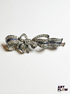 Broche noeud en or blanc 750/°°, diamants et fine ligne de saphirs Poids brut : 9,69gr