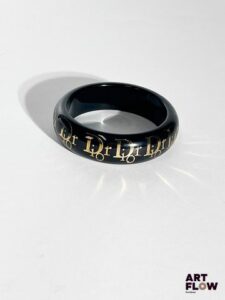CHRISTIAN DIOR Manchette en résine transparente sur fond noir et inscription de la marque dorée. Diamètre : 8 cm