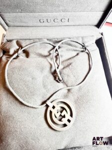 GUCCI Collier pendentif en argent 925/°° de forme circulaire, ajouré figurant le logo de la marque, sur un cordon textile Poids brut : 21,08 gr En l'état Dans son écrin