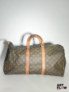 LOUIS VUITTON Modèle Keepall Sac de voyage en toile enduite monogrammée et cuir naturel Dimensions : 25 x 50 x 25 cm Usures : déchirures au zip, taches, traces (voir photos)