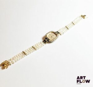 Montre femme en or jaune 750‰ et acier, signée OMEGA De Ville, le cadran de forme rectangulaire à pans coupés bordé de diamants et se terminant par des saphirs calibrés, le bracelet composé de trois rangs de perles également sur or jaune terminé par un fermoir cliquet avec huit de sécurité. Mouvement quartz – Manque la couronne Poids : 19.84 g brut – Longueur : 18.5 cm Diamants : 0.78 carat env. Expertise : Philippine Vanheems