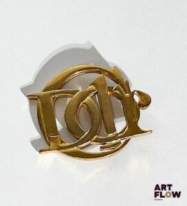 PARFUMS CHRISTIAN DIOR Broche en métal doré, signée au dos. Dimensions : H. 5 x L. 6 cm On y joint deux pins Dior