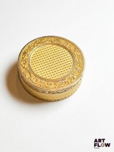 Pilulier en or jaune 750/°°, de forme circulaire, à décor central imitant la vanerie, dans un entourage de frise feuillagée. Poids : 24,85 gr