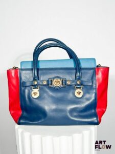 VERSACE Sac à main en cuir dans les tons rouge et bleu orné du logo de la Maison "Médusa" en métal doré Avec bandoulière Dimensions : 26 x 40 cm Usures (voir photos)