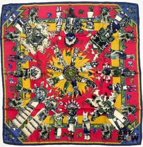 HERMÈS Modèle "Kachinas" d'après un dessin d'Oliver KERMIT Carré en twill de soie dans les tons rouges, jaunes, et bleus 90 x 90 cm Salissures. Avec boîte Bibliographie : Genevieve Fontan, Carrés d'art, Dictionnaire illustré des carrés Hermès valeur, 2025, p.149