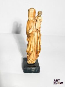 Vierge à l’Enfant en ivoire sculpté en ronde-bosse. Debout, la Vierge tient une colombe dans sa main droite et porte son Fils sur son côté gauche ; la tête ceinte d’une couronne posée sur un voile, elle est vêtue d’une longue robe ceinturée et d’un manteau ouvert dont les pans sont retenus par les avant-bras ; l’Enfant pose sa main droite sur la poitrine de sa Mère et tient l’orbe de l’autre. Fin du XIVe siècle Hauteur : 19 cm Socle en bois noirci (petits accidents, tête de l’Enfant d’époque postérieure) Conformément à la règlementation en vigueur, ce lot sera délivré avec son certificat Intra Communautaire (FR2401300105-K) Provenance : Vente aux enchères du 16 mars 2016, Thierry de Maigret, lot 13 Expertise : Cabinet Fligny