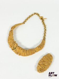 BALENCIAGA Demi-parure composée d'un collier et d'une broche, l'ensemble est recouvert d'un fin cordage doré Le fermoir permet d'ajuster la taille Bon état général malgré une petite tâche Dans une boite