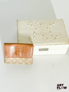 CELINE Ensemble comprenant : – Un coffret blanc, présentant le monogramme Céline en perles blanches, dimensions 16 x 11 x 5 cm, traces d'usure sur les arêtes et angles. – Un porte-monnaie monogrammé. Céline, fermeture bouton-pression, dimensions 8,5 x bon état général malgré quelques traces sur le cuir synthétique, l'intérieur présente des taches.