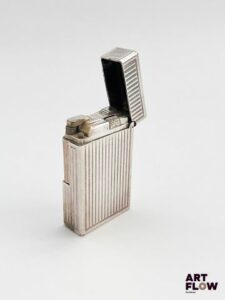 DUPONT Briquet en métal argenté guilloché, monogrammé "L P" sur le côté Dimensions : 3,5 x 5,7 x 1,5 cm Marques d'usure Dans sa boîte