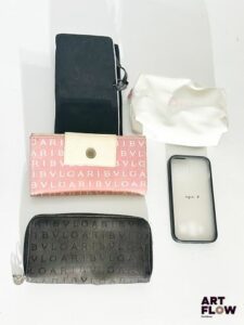 Ensemble comprenant : – BULGARI, un porte-monnaie noir et portefeuille rose, l'ensemble en toile monogrammée – YVES SAINT LAURENT, une trousse de voyage noire et lilas, avec un miroir. — DIOR, une trousse blanche – AGNES B., une coque de téléphone En l'état