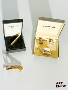 Ensemble comprenant : – PIERRE CARDIN, pince-cravate doré et argenté avec des boutons de manchette argentés, bon état – DIOR, pince-cravate guilloché argenté avec monogramme doré – DIOR, pince-cravate doré, monogrammé "CD", présentant un éclat, dans sa boîte – MUST de CARTIER, pince-cravate doré avec logo, légères marques